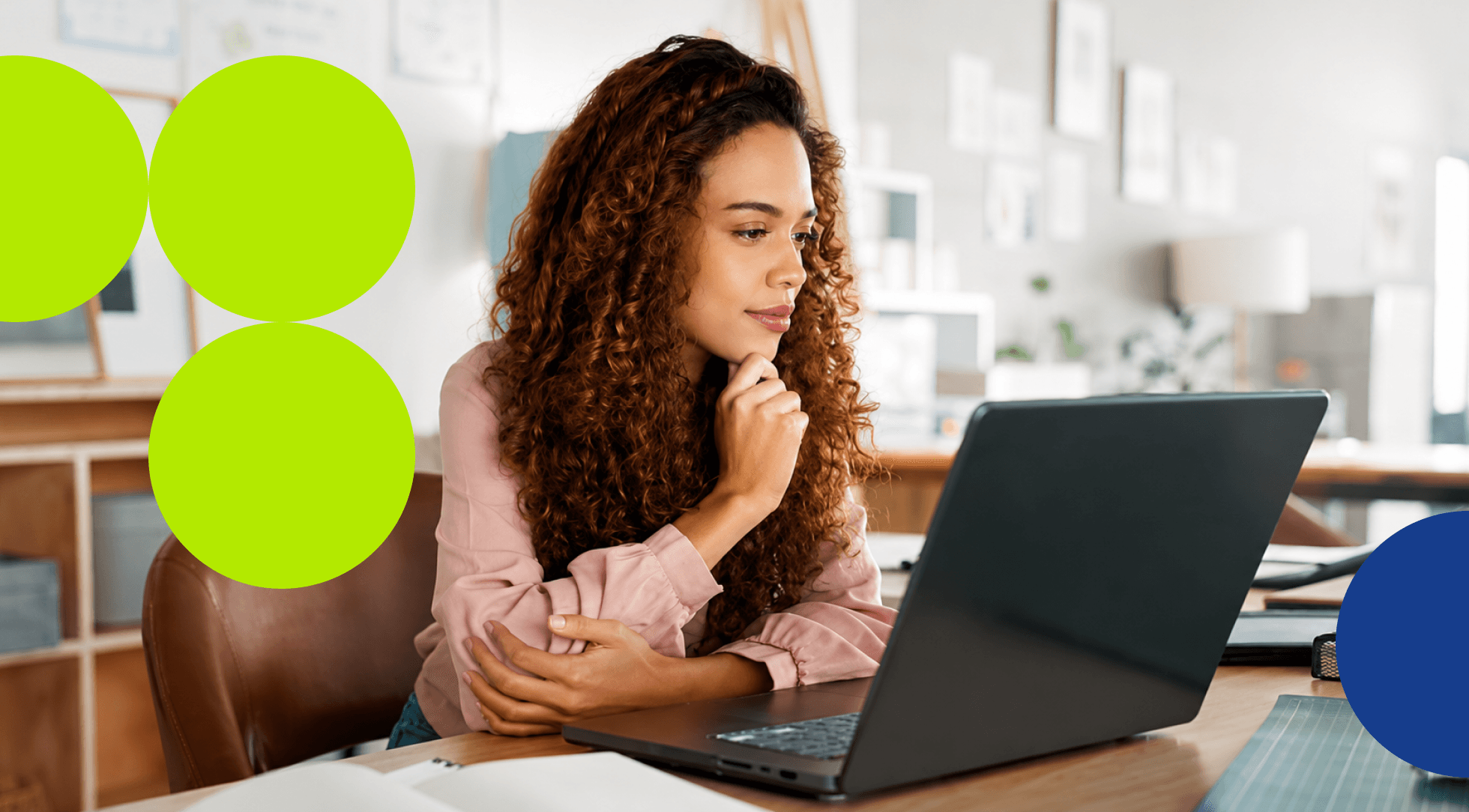 Young woman with curly hair working attentively on a laptop at her desk.